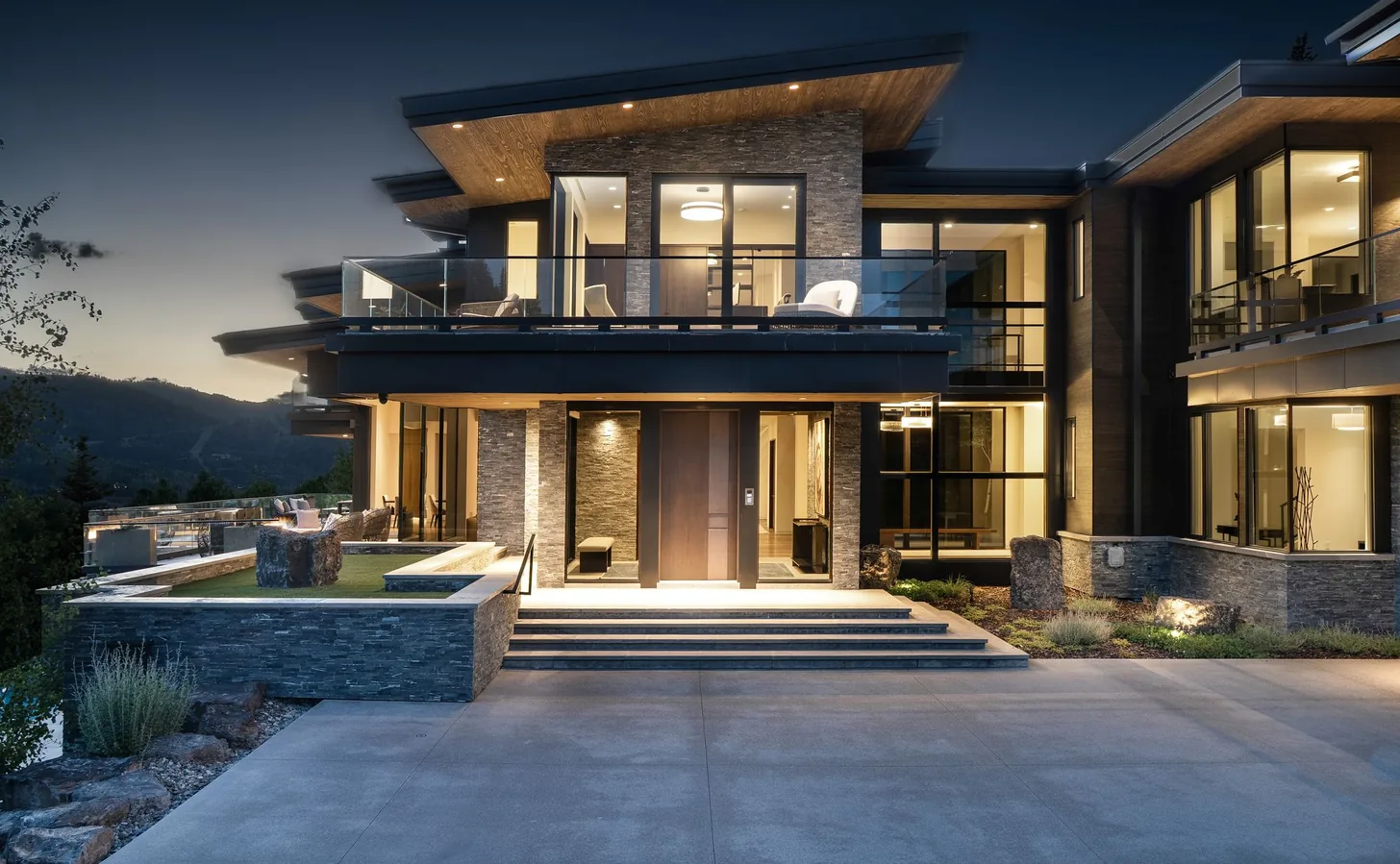 Front elevation at dusk with interiors lit behind stone and glass