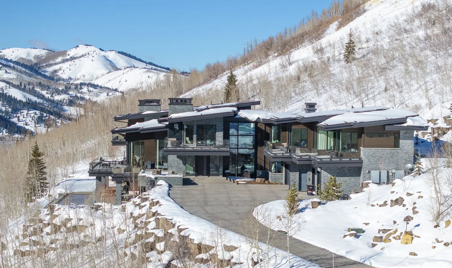 The residence in deep winter, snow on the rooflines and ski terrain rising behind