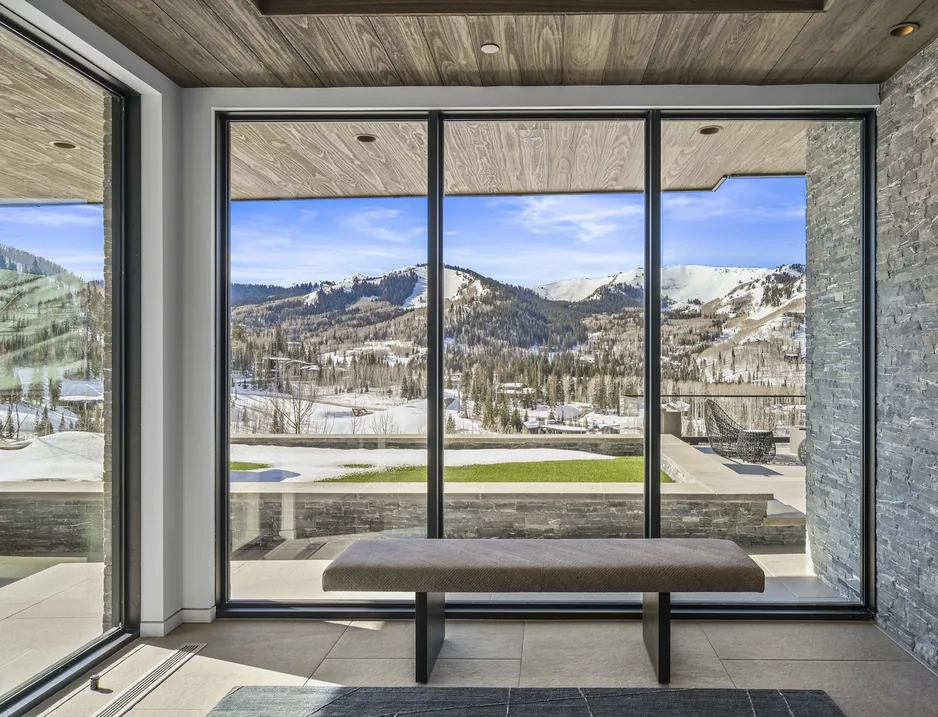 View from inside the residence across snow-covered Colony ski terrain through a floor-to-ceiling window wall