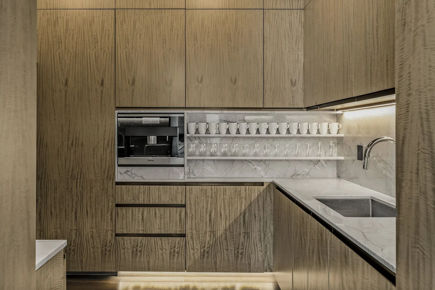 Butler’s pantry in figured wood cabinetry with a marble shelf of glassware and a built-in coffee station