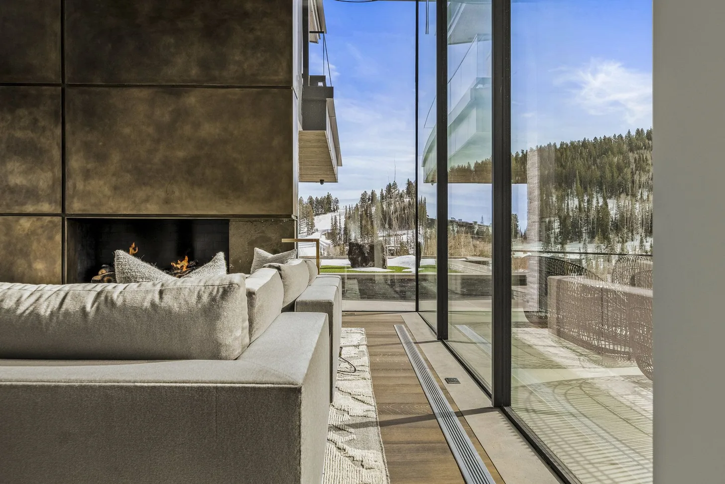 Covered outdoor room with bronze fireplace alight and a glass wall onto the winter mountain