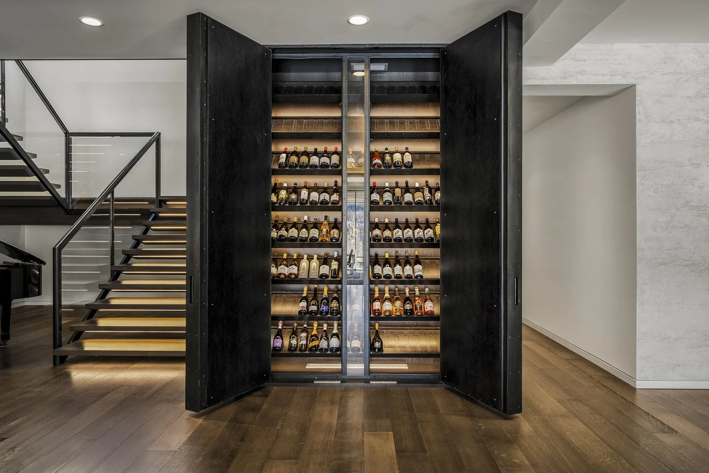 Concealed bar with backlit bottle display opening beside the staircase