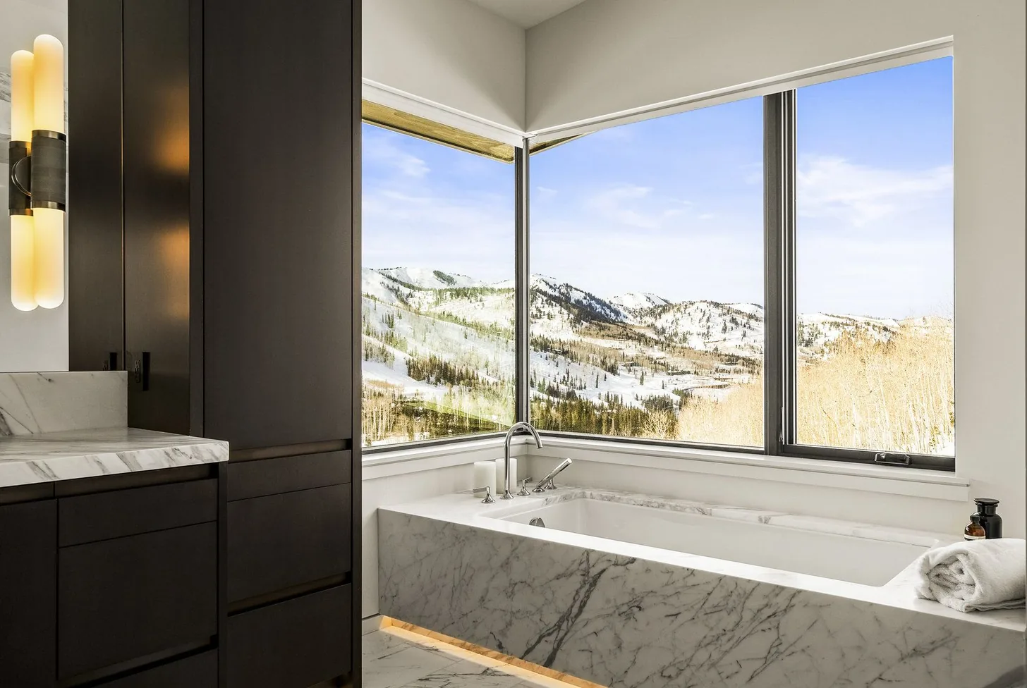 Marble soaking tub beneath a corner window framing snow-covered ski terrain