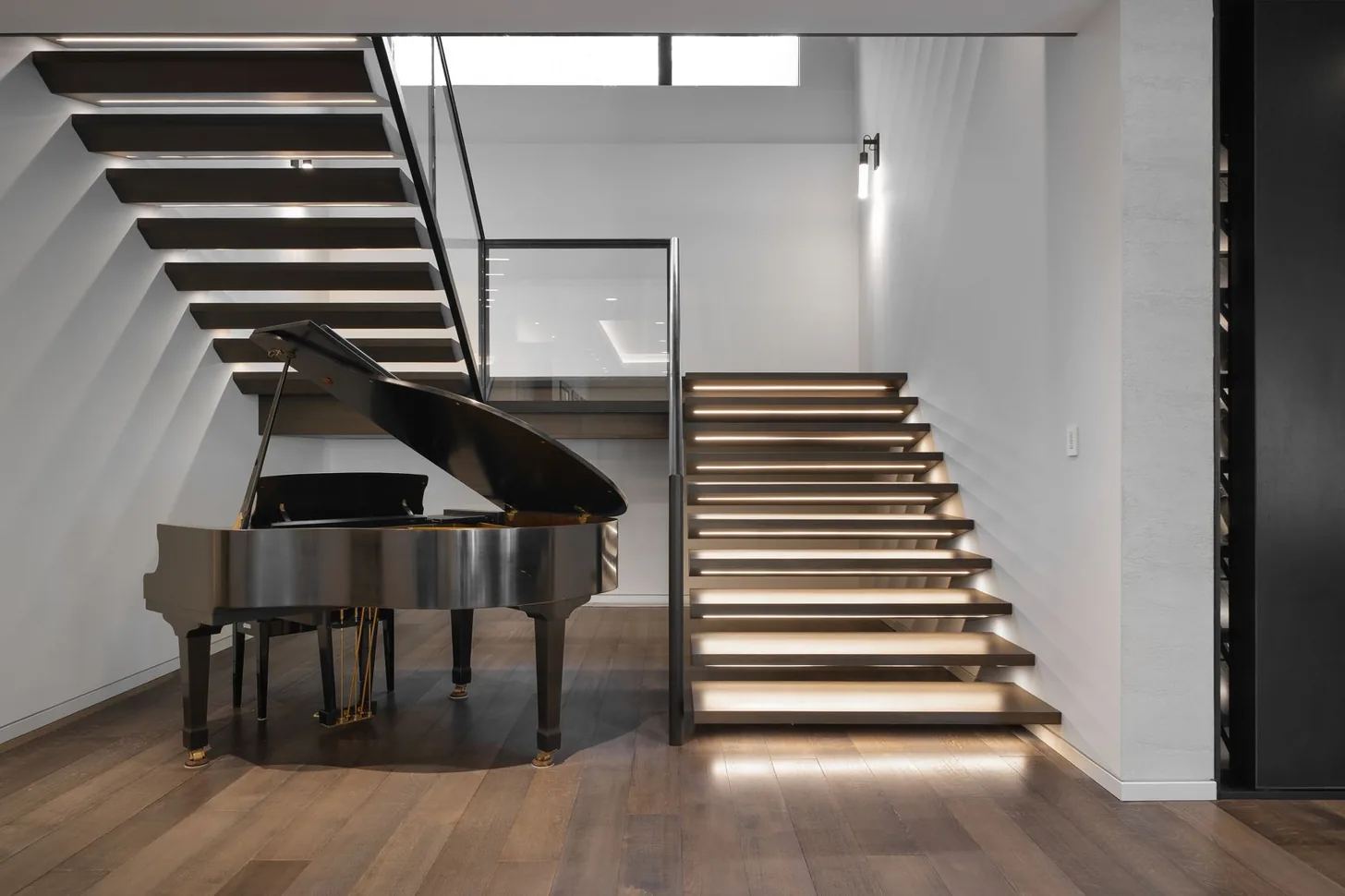 Grand piano beside the backlit floating staircase