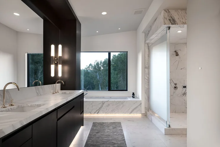 Primary bath with double marble vanity, soaking tub beneath the window and a book-matched marble shower