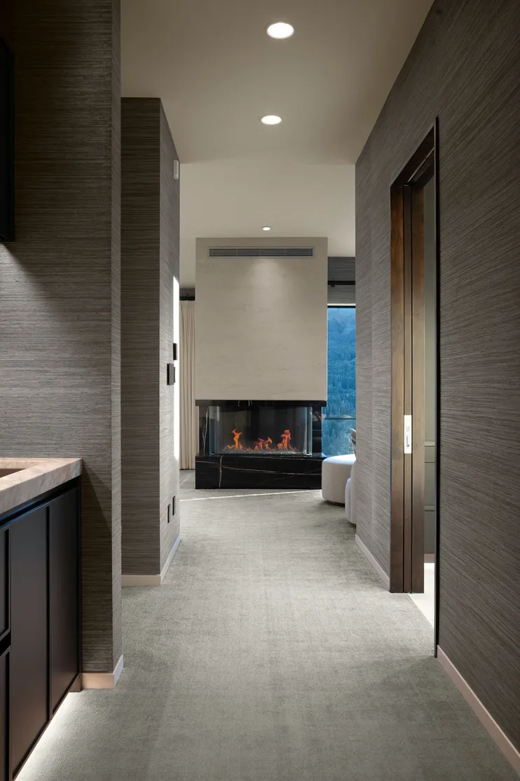 Corridor within the primary suite leading past a marble-clad fireplace to the bedroom beyond