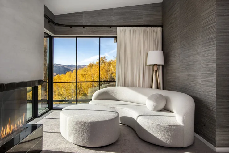 Sitting room within the primary suite with a curved boucle sofa, linear fireplace and glass wall onto golden autumn aspens