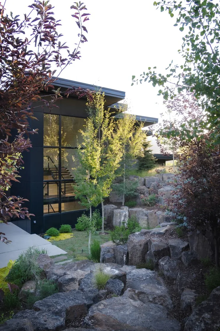 Lava rock garden and ornamental grasses below the dark-clad glass wing of the residence