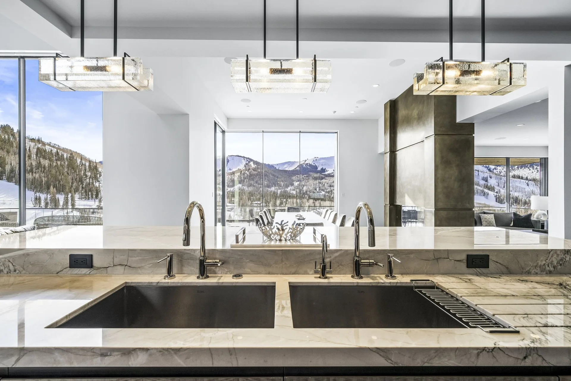 Crystalline pendant fixtures above the marble kitchen island with snow-covered mountains beyond the glass